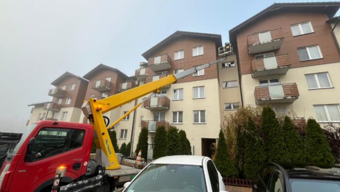 Zadbany budynek mieszkalny z widocznym podnośnikiem koszowym, który może być użyty do przeprowadzenia przeglądów budowlanych.